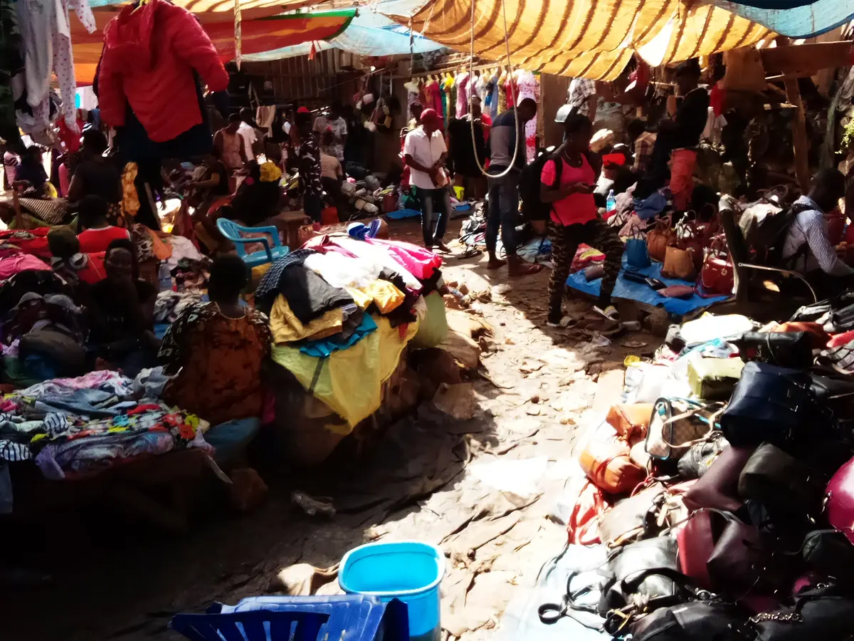 A crowded covered market with piles of clothes and bags and shoppers between the stalls